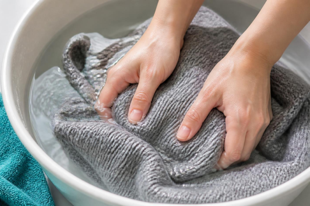 Hands gently pressing a wool sweater under cool water, the safe way to hand wash wool